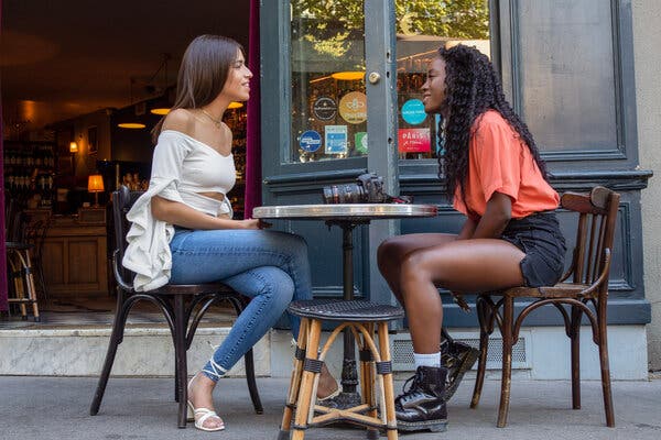 Two women chat while seated at a round table outside of a restaurant.