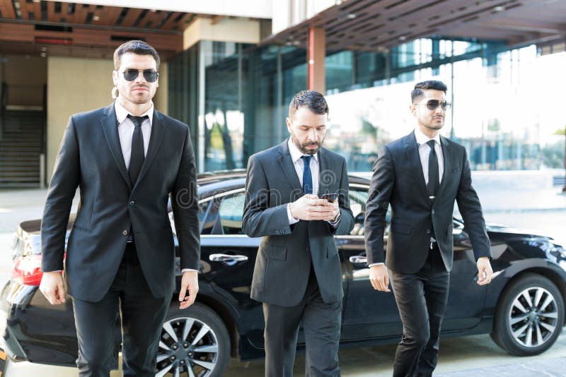young-bodyguards-walking-businessman-service-agents-escorting-entrepreneur-messaging-mobile-phone-campus-138129484.jpg